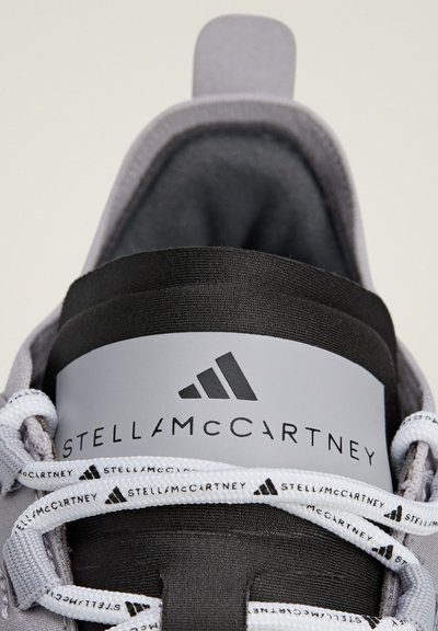 Grey athletic shoe featuring a black band and grey logo, with white laces displaying repeated branding and a cushioned interior.