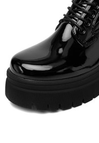 Czarne lakierki z wiązaniem, z grubą, żłobioną podeszwą i zaokrąglonym noskiem, pokazane z bliska na białym tle.