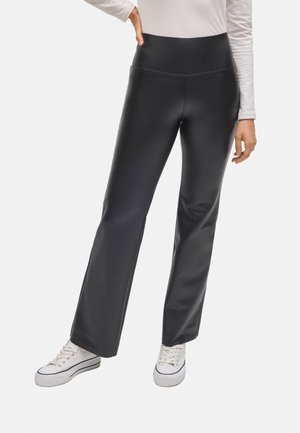 Pantalones de campana negros con una cintura alta, confeccionados en un material suave y elástico. Se combinan con zapatillas blancas para un look casual.