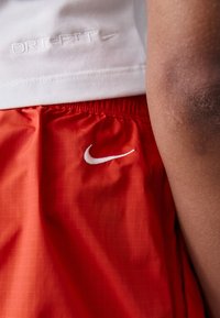Red Dri-FIT shorts featuring a white Nike logo, crafted from lightweight fabric with a grid pattern. Close-up on waistband and fabric texture.