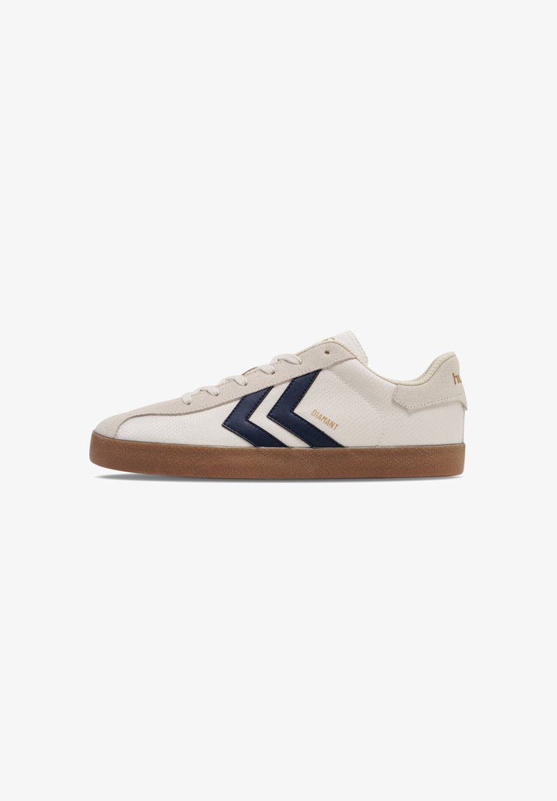 Hvite sneakers med marineblå chevron-detaljer, med en teksturert kanvasoverdel, rund tå og gummisåle. Merkenavnet er synlig på siden.