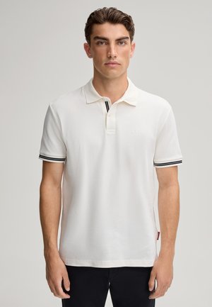 Polo shirt blanc pour homme avec tissu texturé, rayures noires contrastantes au col et aux manches, arborant un petit logo sur la poitrine.