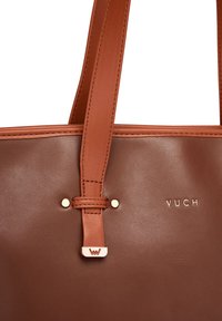 Braune Leder-Handtasche mit glatter Oberfläche, ausgestattet mit goldenen Beschlägen und Branding. Enthält stabile Schulterträger zum Tragen.