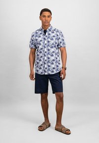 Korte ermes skjorte med blå blomsterdesign, parret med marineblå shorts og brune sandaler. Glatt stoff med kragedetalj.