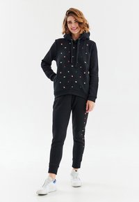 Černá mikina a jogger set s vícebarevnými vyšívanými vzory. Mikina má přední kapsu a nastavitelnou šňůrku.