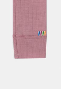 Tissu de leggings rose côtelé avec une petite étiquette rayée arc-en-ciel sur la couture latérale, présentant une texture lisse et un design ajusté.
