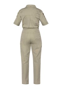 Mono corto de manga corta en color beige con parches de estilo militar en las mangas, detalle de pliegue en la parte trasera, dos bolsillos traseros y pantalones rectos.