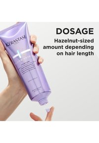 Kérastase Blond Absolu Cicaplash, et lilla rør holdt i en hånd som doserer et kremaktig produkt, merket for en hasselnøttstørrelse mengde.
