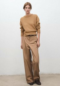 Suéter marrón de punto con cuello redondo, combinado con pantalones de tiro alto color canela y pierna ancha, y zapatos marrón oscuro. Diseño simple y limpio.