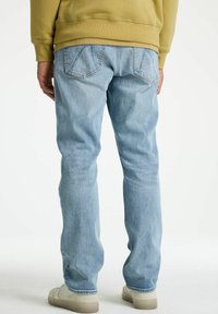 Helle blaue Jeans mit geradem Schnitt, ausgestattet mit Gesäßtaschen und einem verwaschenen Look. Getragen mit einem beigen Hoodie und hellen Schuhen.