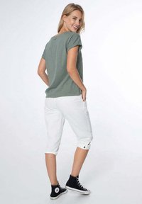 Un t-shirt vert à manches courtes et un pantalon capri blanc. Les pantalons ont des ourlets repliés avec des boutons. Des baskets montantes noires complètent la tenue.