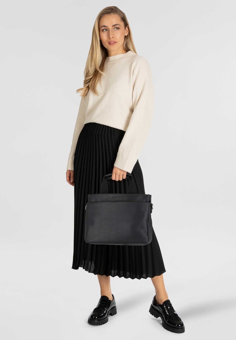 Zwarte leren tas met een gestructureerd ontwerp en een bovenhandvat, gedragen met een crèmekleurige trui en een zwarte geplooide rok, aangevuld met laklederen schoenen.
