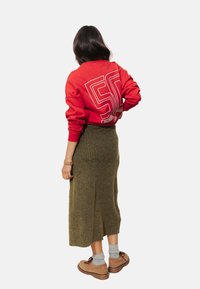 Sweatshirt rouge avec un graphisme blanc au dos, jupe midi côtelée olive, chaussures beiges, chaussettes grises, vue de derrière.