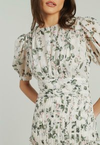 Blumennmusterkleid aus leichtem Stoff mit kurzen Puffärmeln, plissiertem Rock und tailliertem Schnitt, in zarten Pastellfarben und mit grünen Elementen.