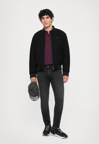 Must musta bomberjakk musta fleecest, millel on kudum collar, kantud maroon polo särk üle. Hallid teksad ja mustad tossud, hoides tumedat halli mütsi.