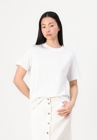 Bílá bavlněná tričko s krátkým rukávem, kulatým výstřihem a volným střihem, v kombinaci se světle barevnou button-up sukní.