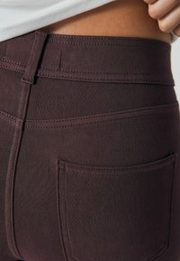 Jeans de denim color burdeos con una vista en primer plano de la cinturilla y el bolsillo trasero, que muestra detalles de costura y una textura suave.