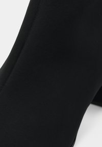Bota preta de tornozelo feita de um tecido liso e texturizado, com bico pontudo e uma silhueta elegante e aerodinâmica. Sem hardware ou detalhes visíveis.
