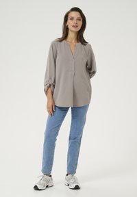 Gray blouse with a V-neck and long sleeves, paired with light blue jeans and white sneakers. Smooth texture, relaxed fit, no patterns.