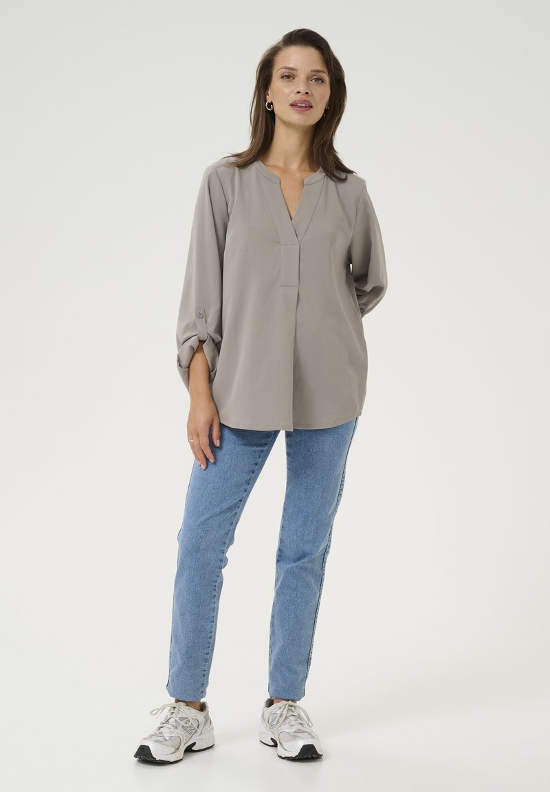 Gray blouse with a V-neck and long sleeves, paired with light blue jeans and white sneakers. Smooth texture, relaxed fit, no patterns.