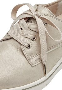 Sneaker in pelle beige con finitura lucida, dotato di lacci beige chiaro e occhielli metallici rotondi. Suola bianca con sottili accenti argentati.