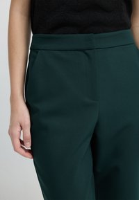 Pantaloni su misura verdi con una texture liscia, dotati di una vita piatta, tasche laterali e un design con gamba dritta.