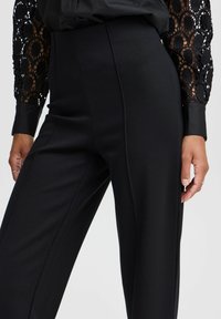 Schwarze maßgeschneiderte Hose mit glatter Textur, hoher Taille, geraden Beinen und dezenten Vordernähten. Elegantes und figurbetontes Design.