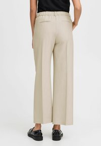 Beige wide-leg trousers with a textured finish, elastic waistband, and two back pockets, paired with black flat shoes.