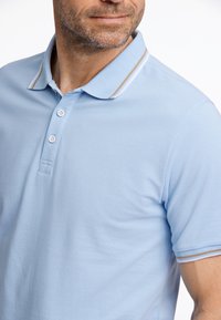 Polo de color azul claro hecho de tela texturizada. Presenta un cuello con solapa, tres botones y detalles a rayas en contraste en el cuello y las mangas.