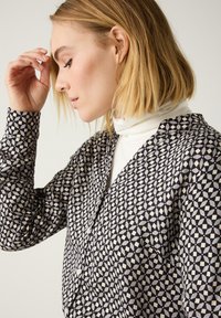 Zwart-wit gebloemde blouse met geometrische vormen; heeft een kraag, knoopsluiting aan de voorkant en lange mouwen met een getailleerd silhouet.