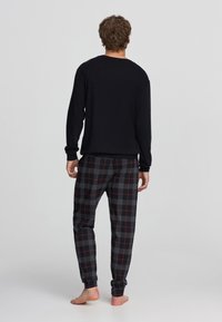 Maglia nera a maniche lunghe abbinata a pantaloni da pigiama a quadri grigi con dettagli rossi. I pantaloni presentano una vita elastica e polsini aderenti.