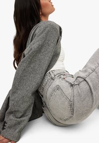 Gray herringbone jacket with oversized sleeves, worn over a white top and high-waisted gray jeans with red accents and stitching.
