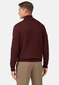 Maglione a maglia bordeaux con colletto alto, polsini e orlo a coste. Texture liscia, design aderente e retro semplice. Indossato con pantaloni di colore chiaro.