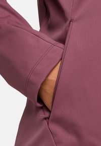 Giacca a maglione di un morbido colore viola chiaro, dotata di una tasca frontale con zip e sottili dettagli di cucitura ai polsini.