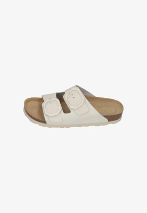 White slide sandal featuring two adjustable straps with octagonal buckles, a cork footbed, and a textured rubber sole.