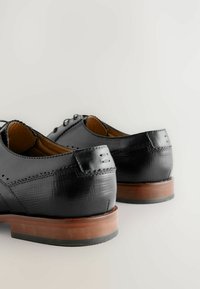 Zwarte leren schoenen met een gestructureerde afwerking, vetersluiting, houten hak en decoratieve stikdetails. Heeft perforaties aan de zijkanten.
