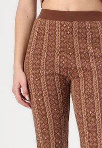 Barna mintás leggings, geometrikus dizájnnal, gyémántokkal és vonalakkal, gumis derékrész és puha szövettextúra.