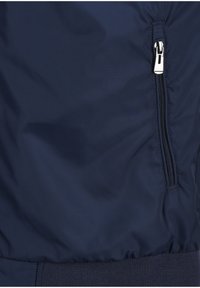Navy blue nylon bomber jacket fabric featuring a zippered pocket and ribbed waistband texture. Smooth finish with minimal sheen.