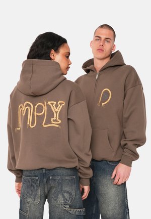 Brown hoodie featuring embossed rope-like gold lettering on the back and a zippered front, paired with blue denim pants.