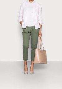 Camicia a righe rosa chiaro, T-shirt bianca, pantaloni verde oliva arrotolati, décolleté nude e borsa beige. Materiali morbidi, vestibilità su misura.