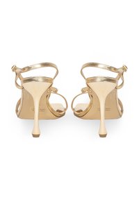 Złote sandały na wysokich obcasach z cienkimi paskami w kostce, eleganckim, zwężającym się obcasem i gładkim metalicznym wykończeniem.