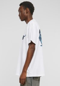 Hvid bomulds t-shirt med løs pasform; har et grafisk tryk i blå på ryggen og en rund halsudskæring; korte ærmer, afslappet stil.