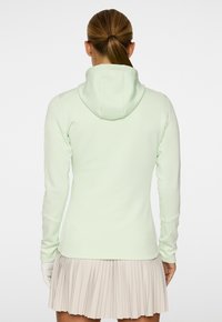 Felpa con zip color verde menta, cappuccio e maniche lunghe. Tessuto morbido con elasticità. Presenta un piccolo logo nella parte posteriore del colletto.