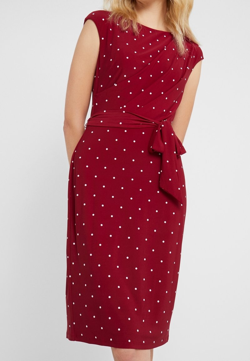 Robe bordeaux à motif à pois. Dotée de manches courtes, d'un design ajusté, d'une ceinture à la taille et d'un ourlet au genou. Tissu lisse et extensible.