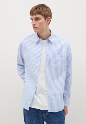 Camicia button-up a righe blu chiaro e bianche con colletto a punta e taschino sul petto, indossata su una maglietta bianca, taglio casual.