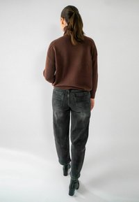 Pull à col roulé en tricot marron, coupe décontractée, associé à un jean gris foncé fuselé et des bottines à talons blocs noires.