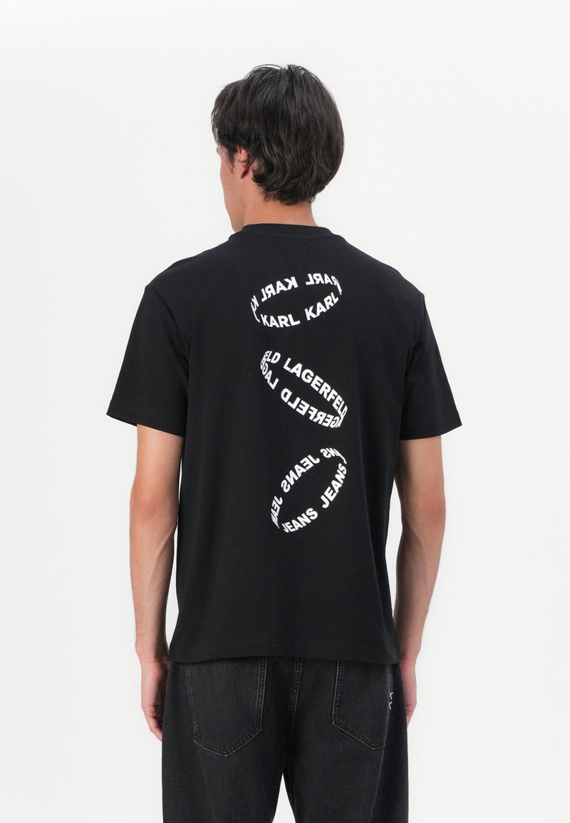 Zwart katoenen T-shirt met een cirkelvormig wit tekstontwerp op de achterkant. Korte mouwen en een klassieke ronde hals. Eenvoudige en moderne snit.