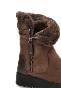 Botas de tobillo de ante marrón con forro de pelo sintético, detalle de cremallera en el lateral y suela de goma negra texturizada. Puño doblado para mayor calidez.