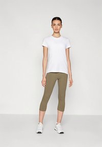 Valgete lühikeste varrukatega t-särk, kombineeritud oliivroheliste pahkluu pikkuste retuusidega, kantud valgete spordijalatsitega. Lihtne disain, sile pind.