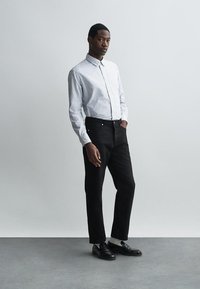 Svītrains pogu krekls baltā un zilā krāsā, apvienots ar melnām biksēm. Apģērbs ir ar pielāgotu griezumu un melnām kurpēm, lai radītu kontrastu.